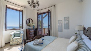 A bedroom with a bed, a dresser, a chair, and a view of the sea. - Villa Ai Venti 8, Emma Villas (Massarosa)
