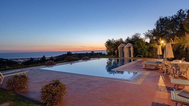 A swimming pool with a view of the sea at sunset, surrounded by outdoor seating and a small gazebo. - Villa Ai Venti 8, Emma Villas (Massarosa)
