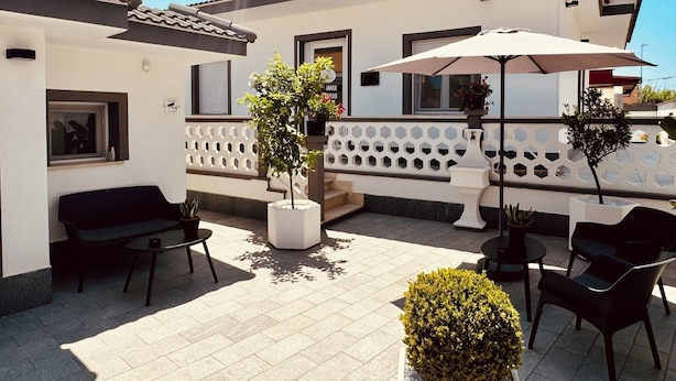 Un espace patio aménagé avec des meubles d’extérieur, des plantes en pot et une rambarde blanche.