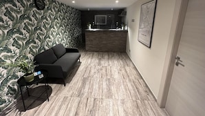 Un espace d’accueil moderne avec un comptoir de réception en bois, un canapé noir et une horloge murale.