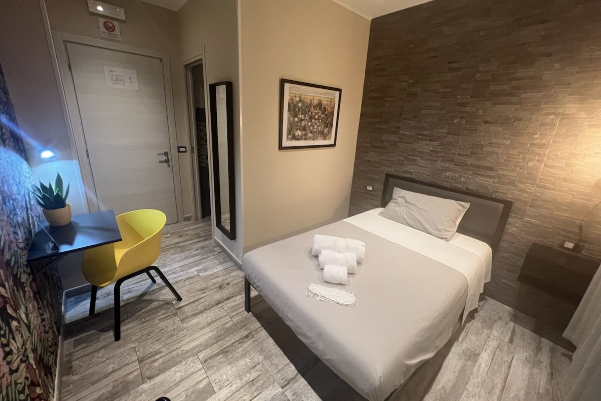 A hotel room with a bed, a desk, a chair, and a potted plant.