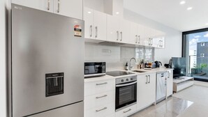 A modern kitchen with stainless steel appliances, white cabinetry, and a large window offering a view of the city. - The CityScape Apartment with Wi-Fi and Balcony (Auckland CBD)