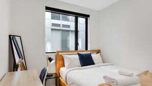 A modern bedroom with a wooden bed, white bedding, a window with blinds, a desk with a chair, and a framed picture on the wall. - The CityScape Apartment with Wi-Fi and Balcony (Auckland CBD)