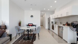 A modern kitchen with white cabinets, a microwave, and a dishwasher. There is a dining area with a round table and two chairs. - The CityScape Apartment with Wi-Fi and Balcony (Auckland CBD)