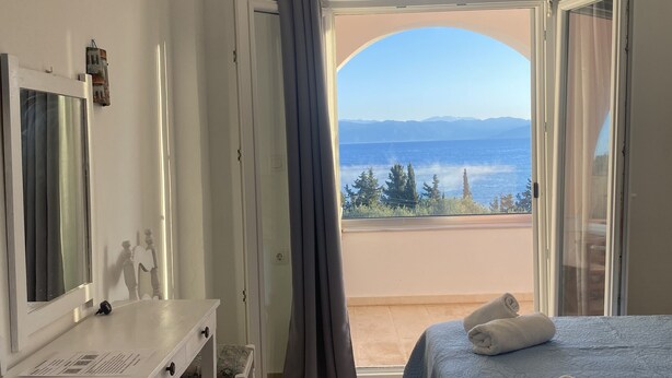 A hotel room with a desk, two beds, a large window with a view of the sea and mountains, and an air conditioning unit. - Panorama Notos (Corfu)