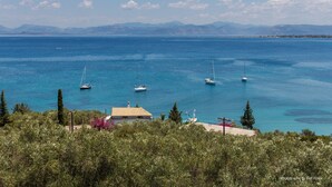 A coastal view with boats on the water, a building with a red roof, and mountains in the background. - Panorama Notos (Corfu)