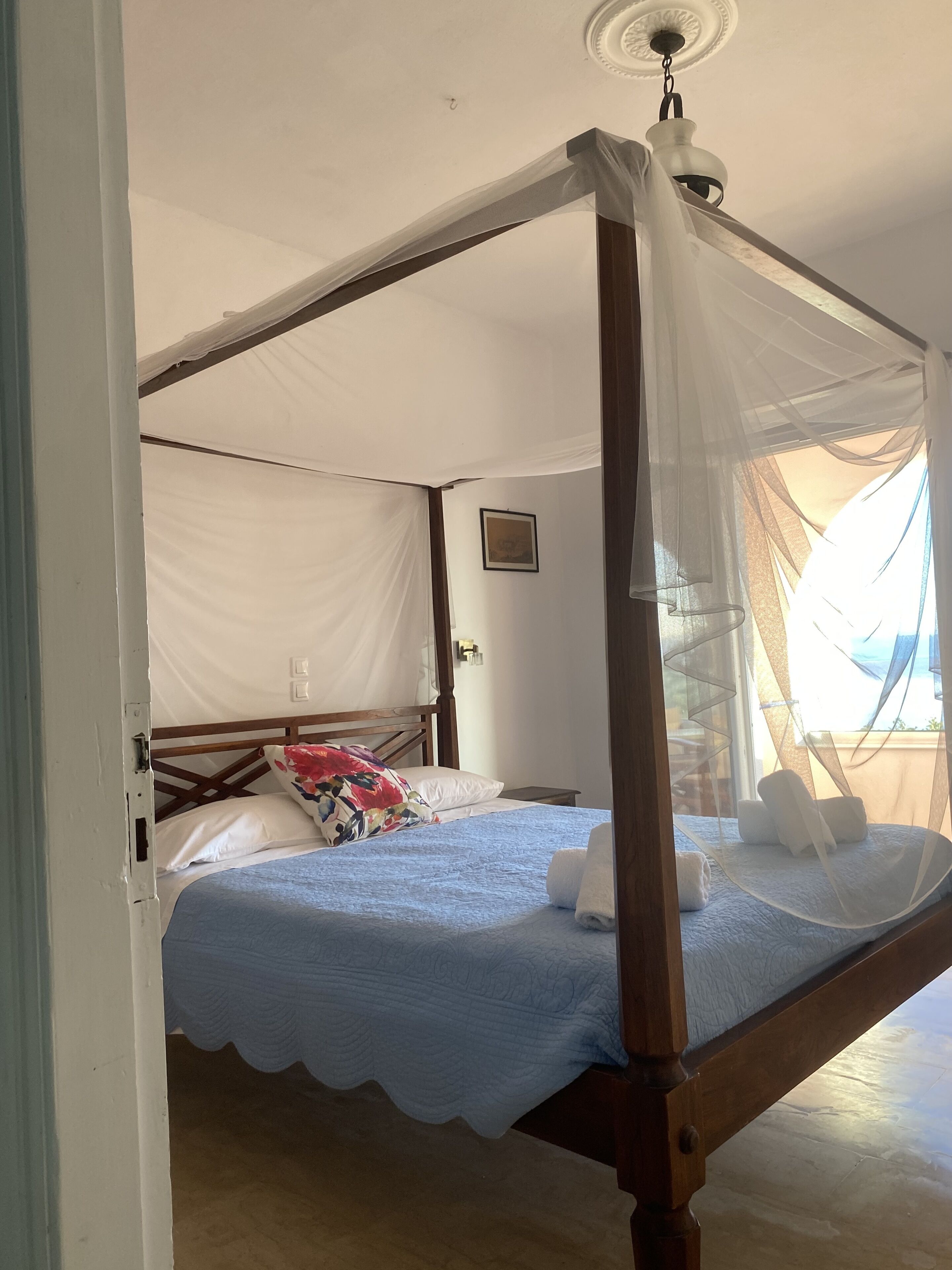 Un dormitorio con una cama con dosel, un dosel, una mesita de noche y una ventana con vistas.