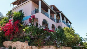 A two-story building with a pink facade, blue balconies, and arched windows. - Panorama Notos (Corfu)