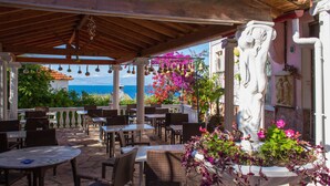 An outdoor patio with tables and chairs, a decorative fountain, and a view of the sea. - Panorama Notos (Corfu)