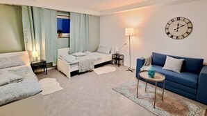 Una habitación de hotel moderna con una cama, un sofá azul, una mesita con una lámpara y un reloj de pared.