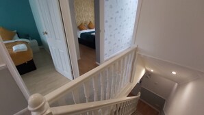 A staircase leading to a bedroom with a bed, a nightstand, and a window with a moon and star pattern.