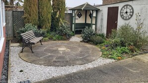 A courtyard with a circular stone patio, a wooden bench, and a small gazebo.