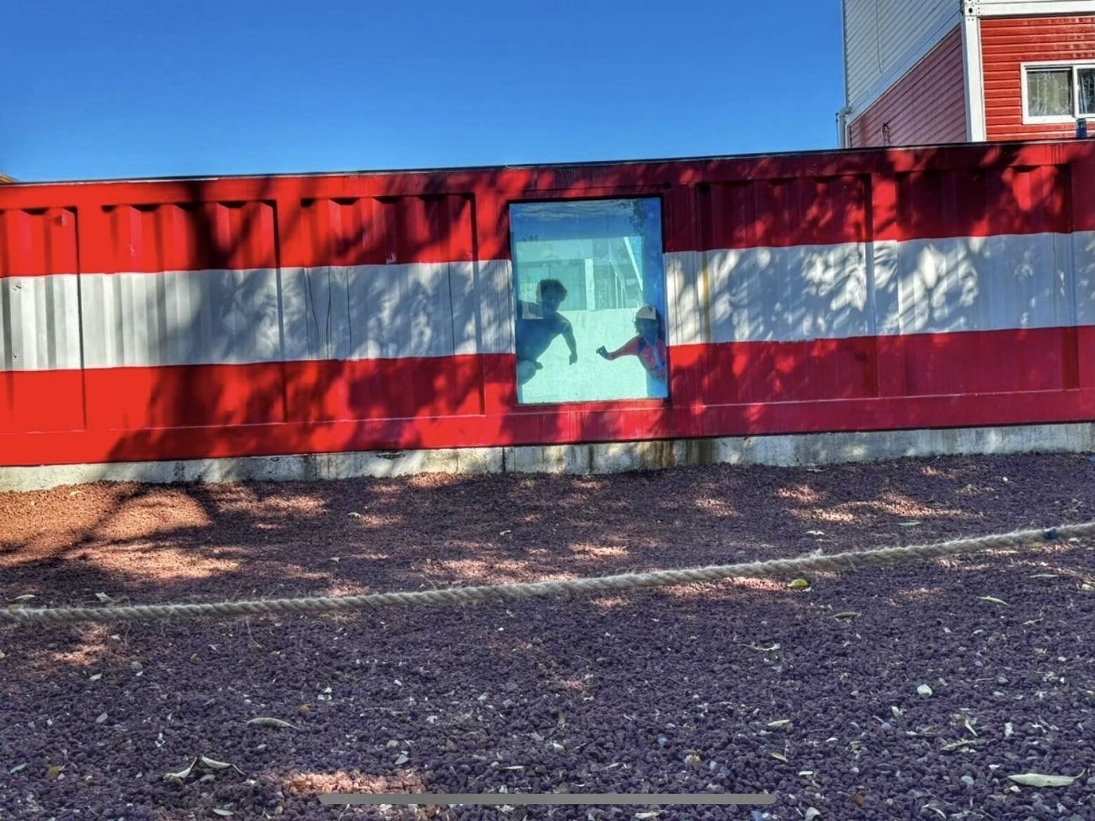 A red and white striped wall with a window displaying two children playing.