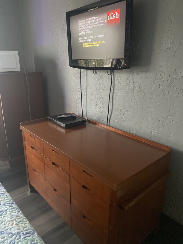 A flat-screen TV mounted on a textured wall, with a wooden dresser below.