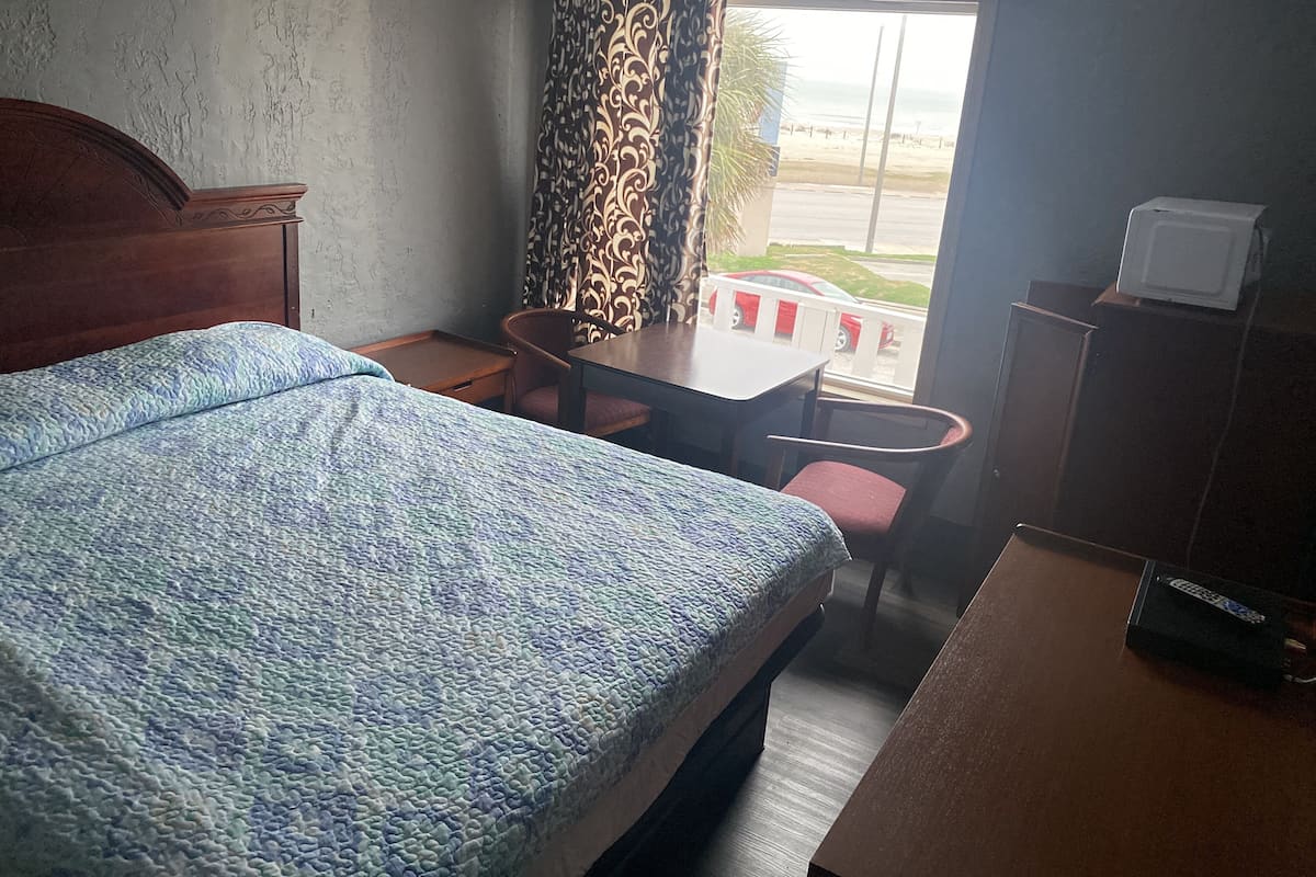 A hotel room with a bed, a table, two chairs, a TV, and a view of the beach.