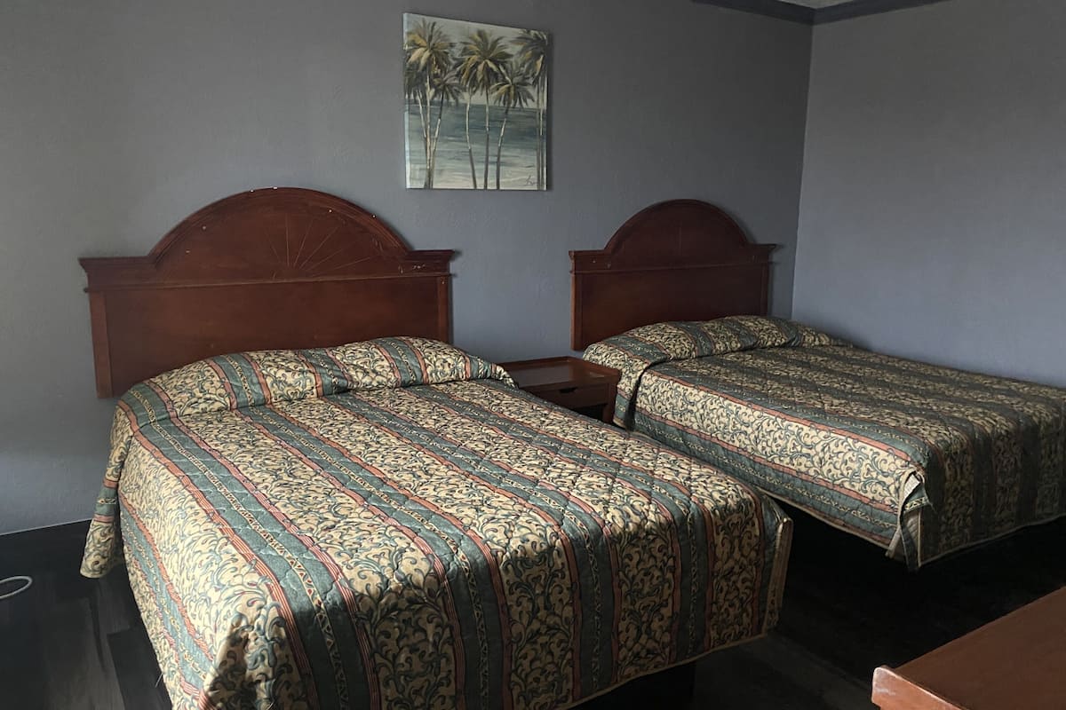 A room with two single beds, each with a wooden headboard, a small bedside table, and a patterned bedspread.