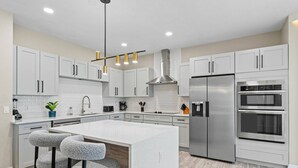 Une cuisine moderne avec des meubles blancs, des appareils en acier inoxydable et un îlot central doté de tabourets de bar.