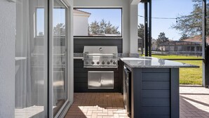 Un espace cuisine extérieur doté d’un barbecue encastré et d’un petit réfrigérateur.