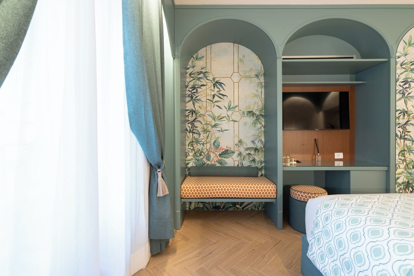 Ein modernes Hotelzimmer mit Holzboden, einem Bett mit gemusterten Betttextilien, einer Bank mit einem gemusterten Kissen, einem Fernseher und einer Wand mit Bambus-Wandgestaltung.