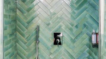 A shower with a herringbone tile pattern and a handheld showerhead.