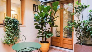 A patio area with a table and chairs, a potted plant, and a wooden door with glass panels. - La Dimora del Mercante (Florence)