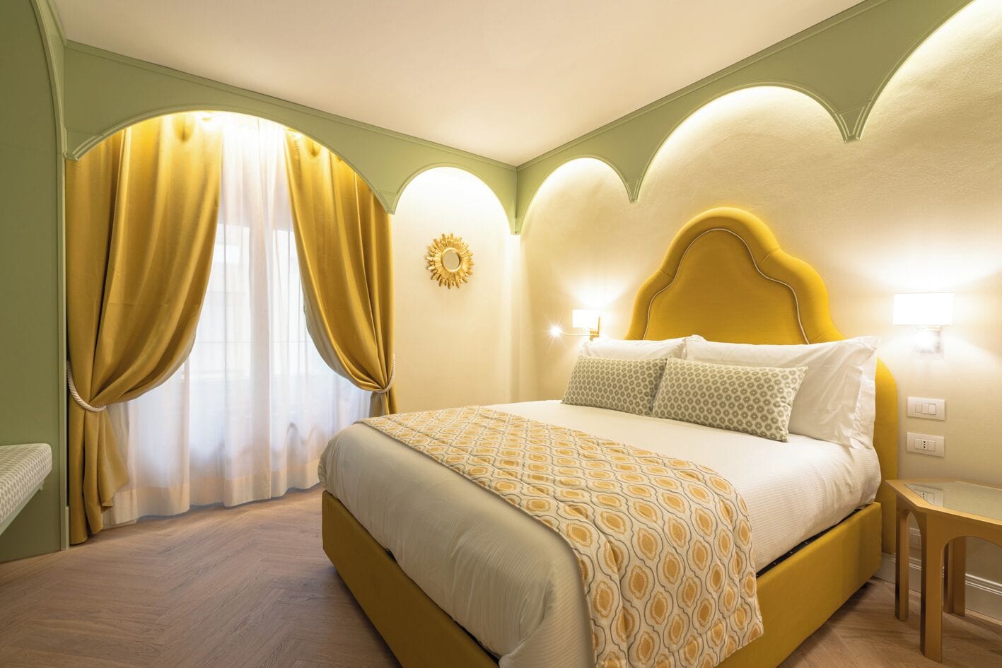 Ein Hotelzimmer mit Bett, Vorhängen, einem wandmontierten Spiegel und einem Nachttisch.
