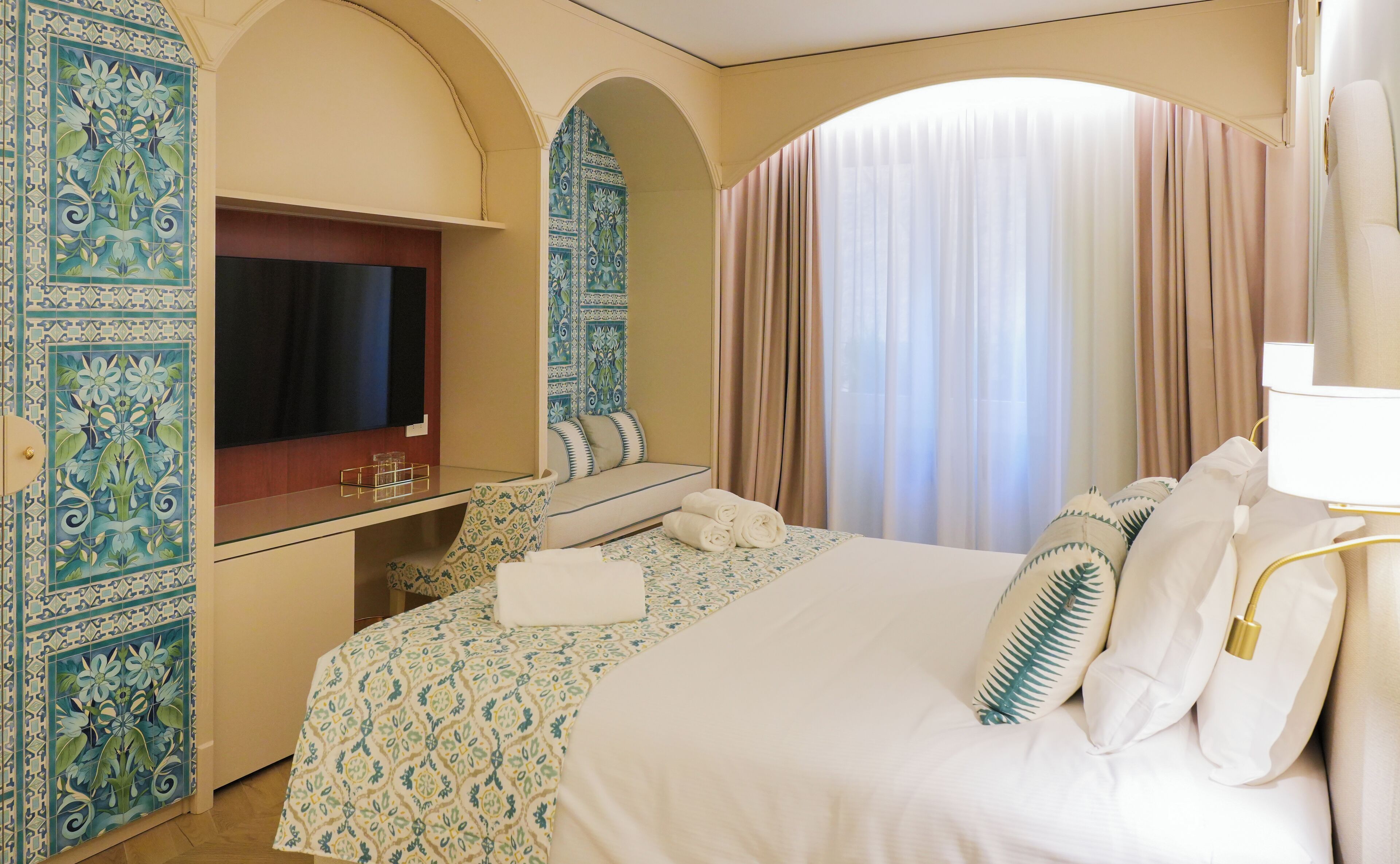 Ein Hotelzimmer mit Fernseher, Schreibtisch, Bett mit gemusterten Textilien und dekorativen Fliesen.