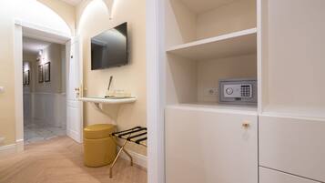A hallway with a flat-screen TV mounted on the wall, a small vanity with a mirror, and a security safe on a shelf.