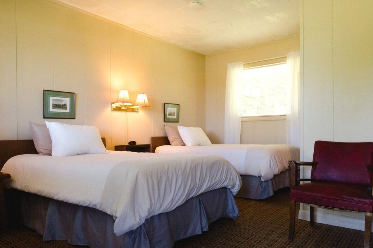 A hotel room with two beds, a red chair, and two wall-mounted lamps.