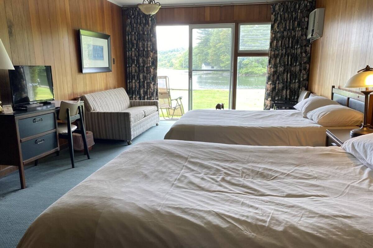 A hotel room with two beds, a desk with a television, a chair, and a view of a lake through the window.