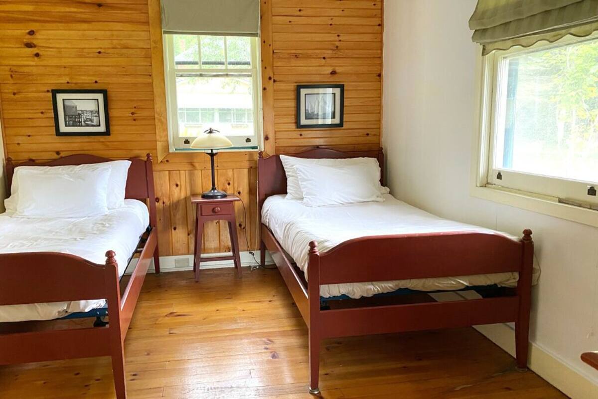 A room with two wooden beds, a nightstand with a lamp, and framed pictures on the walls.