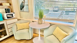 A cozy living room with two armchairs, a small round table, a microwave, and a window with blinds.
