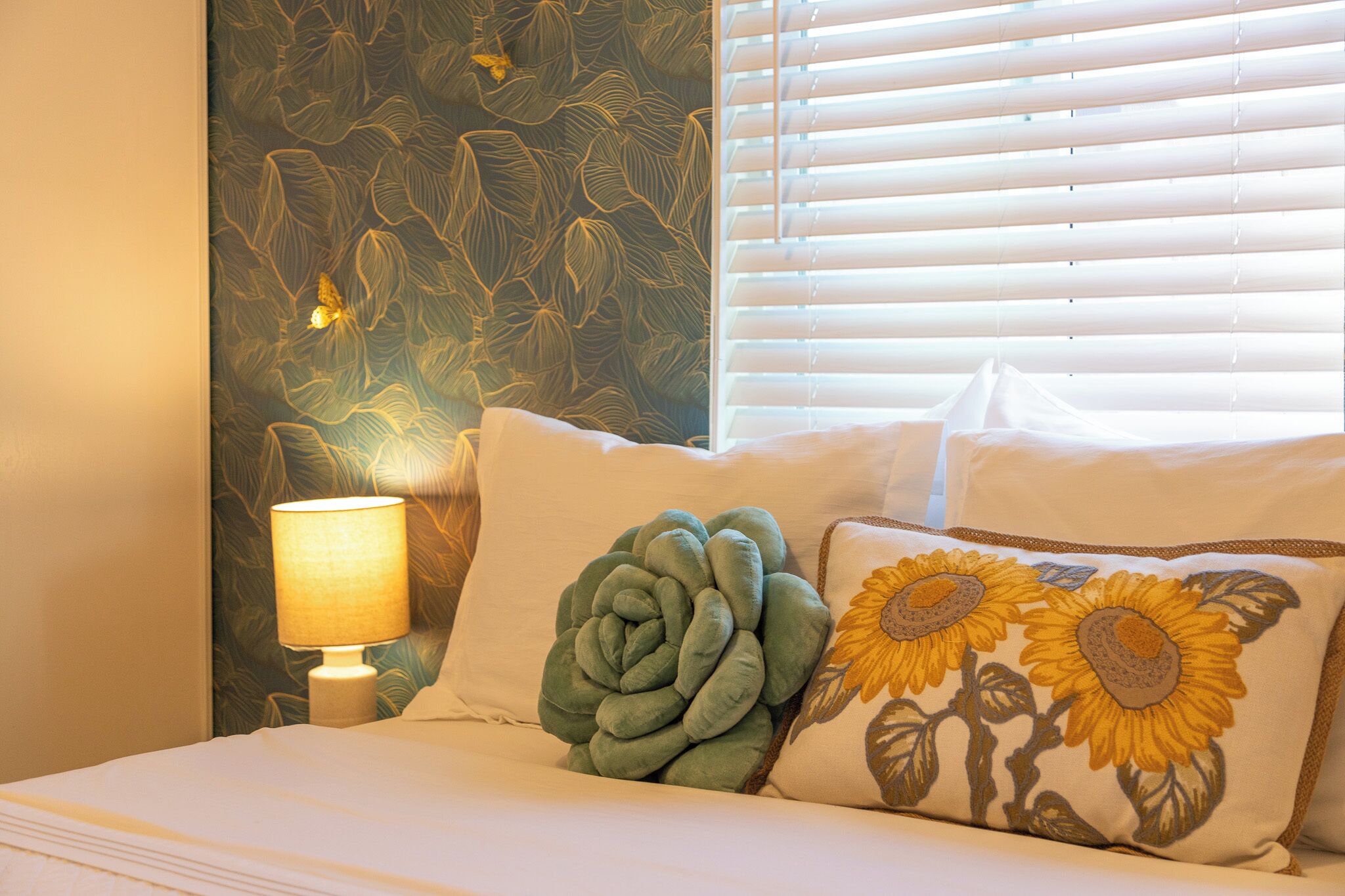 Ein Bett mit weißer Bettwäsche, einem grünen Zierkissen und einem Kissen mit Sonnenblumenausstickung.