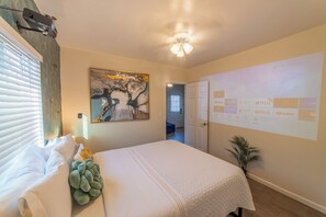 A bedroom with a bed, a projector screen displaying streaming services, a ceiling fan, and a painting on the wall.