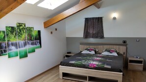 Een slaapkamer met een houten bed, een nachtkastje, een wandlamp en een raam met uitzicht op bomen.