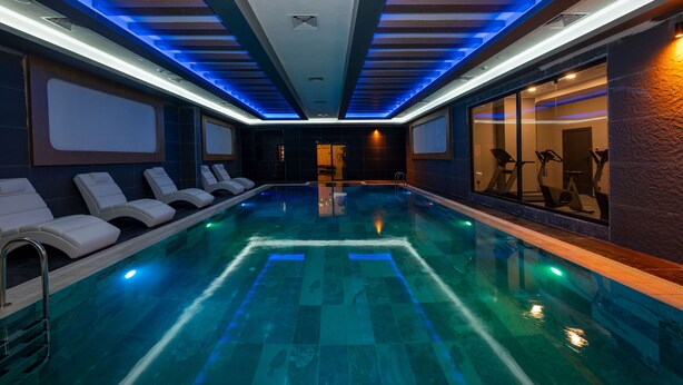 A modern indoor swimming pool with blue lighting, lounge chairs, and exercise equipment. - The Nirvanas Hotel (Istanbul)