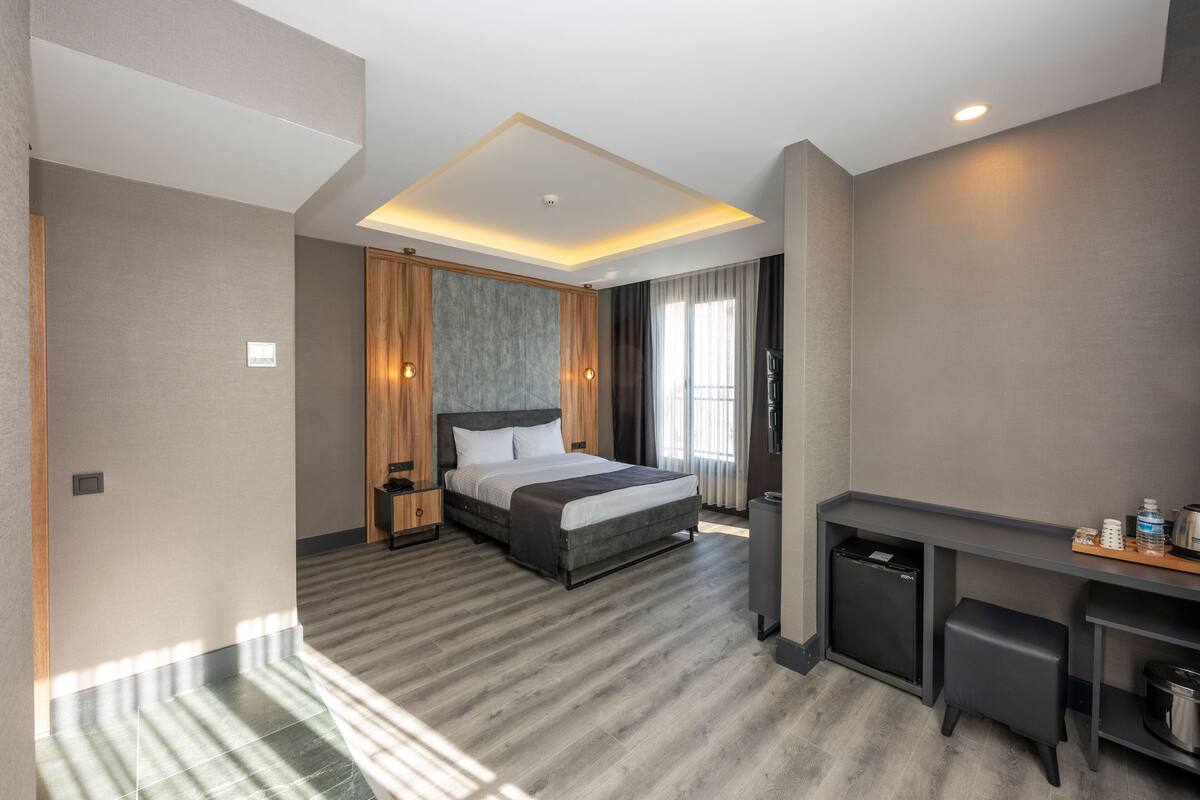 A modern hotel room with a large bed, a desk, and a small kitchenette.