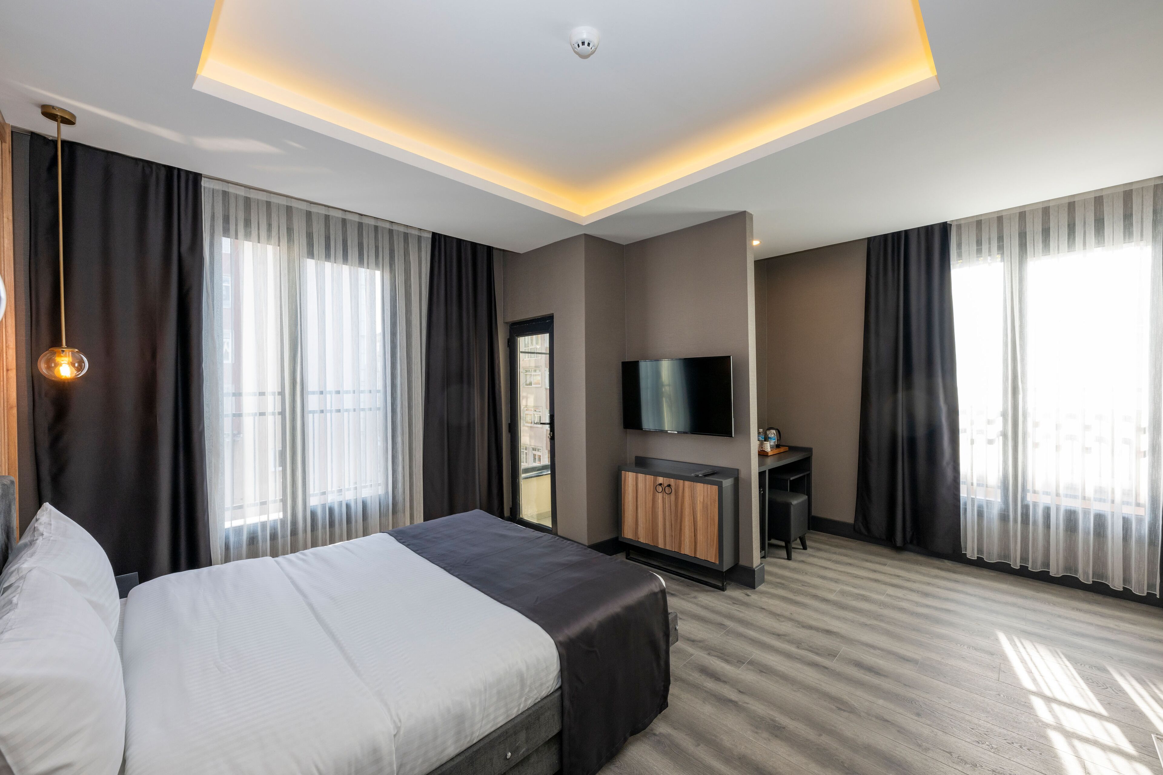 A modern hotel room with a large bed, a desk, a flat-screen TV, and a ceiling light fixture.