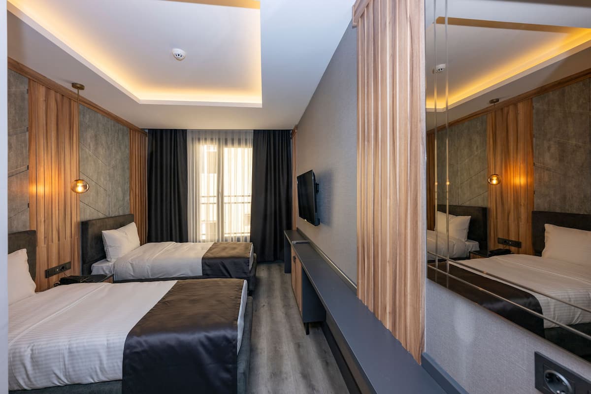 A hotel room with two beds, a TV, a mirror, and a window with curtains.