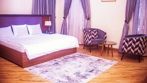 A bedroom with a large bed, a small round table, two chairs, and a patterned rug.