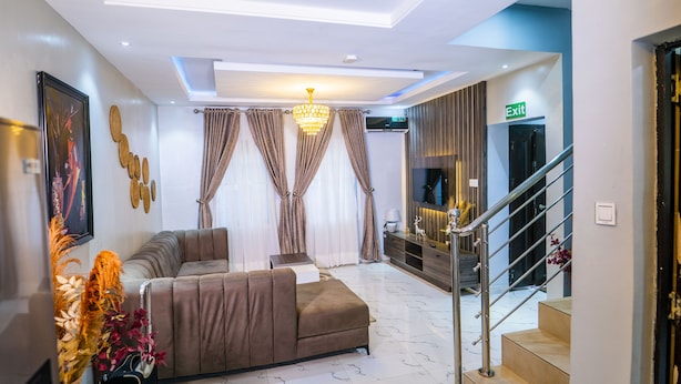 A modern living room with a sectional sofa, a chandelier, a flat-screen TV, and a staircase.