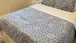 A bedroom with a patterned bedspread, a nightstand with a lamp, two windows, and a colorful abstract painting on the wall. - Modern private One bedroom apartment Calgary Downtown #502 (Calgary)