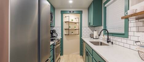 A modern kitchen with teal cabinets, a stainless steel refrigerator, a built-in oven, and a white countertop with a sink and faucet.