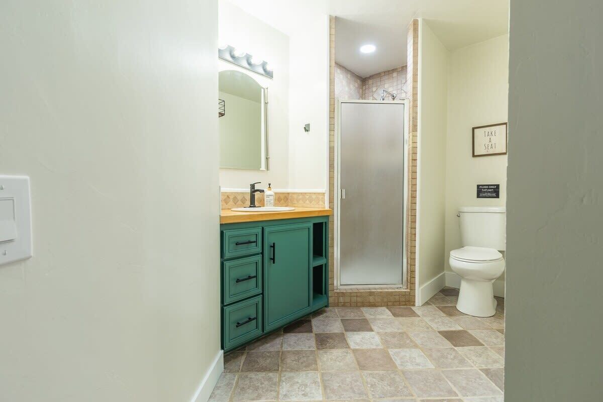 A bathroom with a green vanity, a shower, and a toilet.
