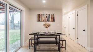 A dining area with a table set for four, benches, a vase with dried flowers, and a colorful abstract painting on the wall. - Centrally Located Family Home, Backyard w Firepit! (Meridian)