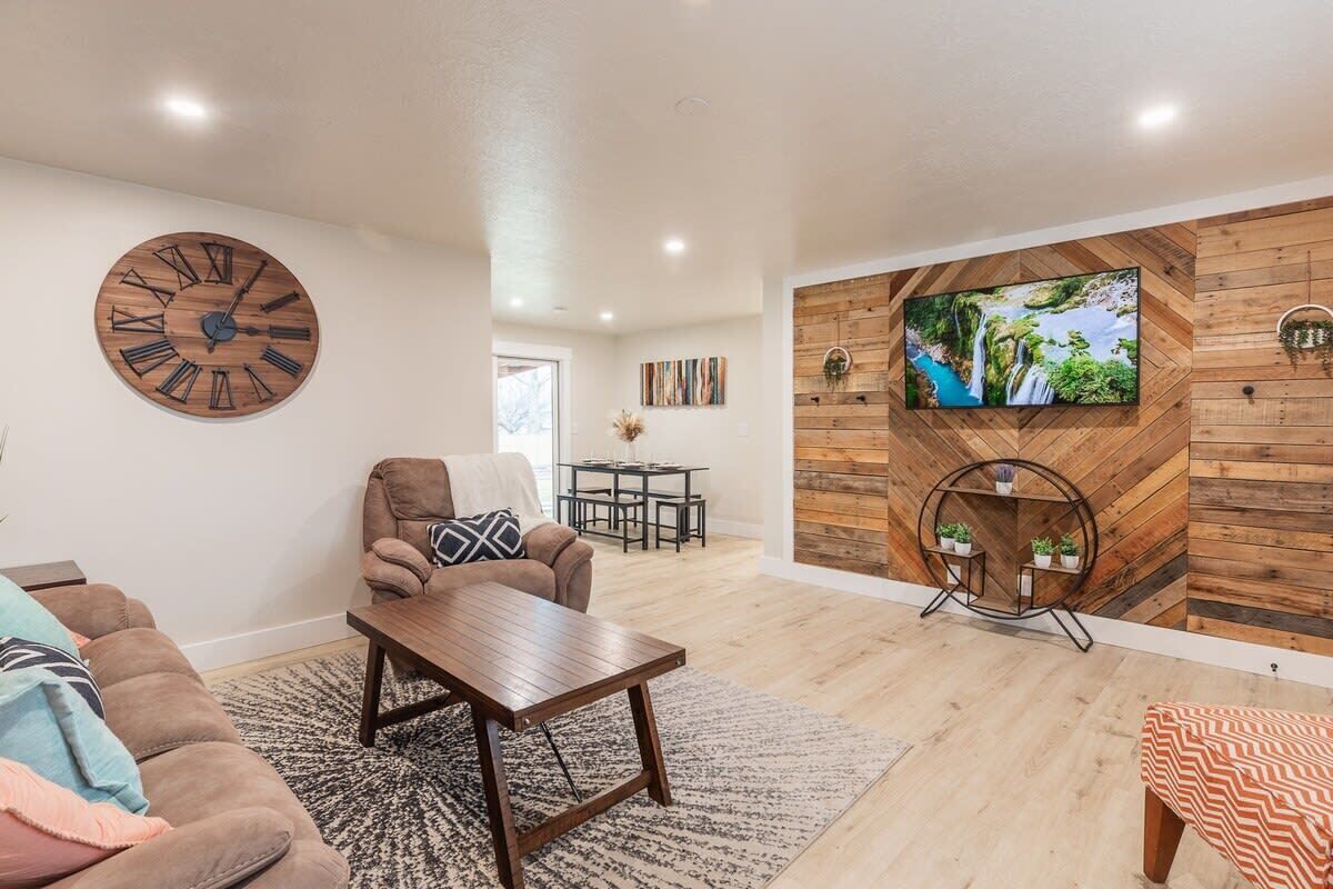A modern living room with a large wooden clock, a comfortable sofa, a coffee table, and a TV mounted on a wooden wall.
