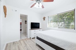 A bedroom with a bed, a television, a ceiling fan, and a window with blinds. - Walk to Beach | Sleeps 8 | Firepit | Beachcombers Nook | Panama City Beach (Panama City Beach)