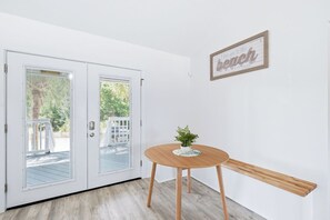 A room with a wooden bench, a small table with a plant, and a door with glass panels. - Walk to Beach | Sleeps 8 | Firepit | Beachcombers Nook | Panama City Beach (Panama City Beach)