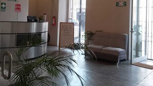 Un vestíbulo de hotel con una recepción, un sofá, plantas en macetas y un candelabro.