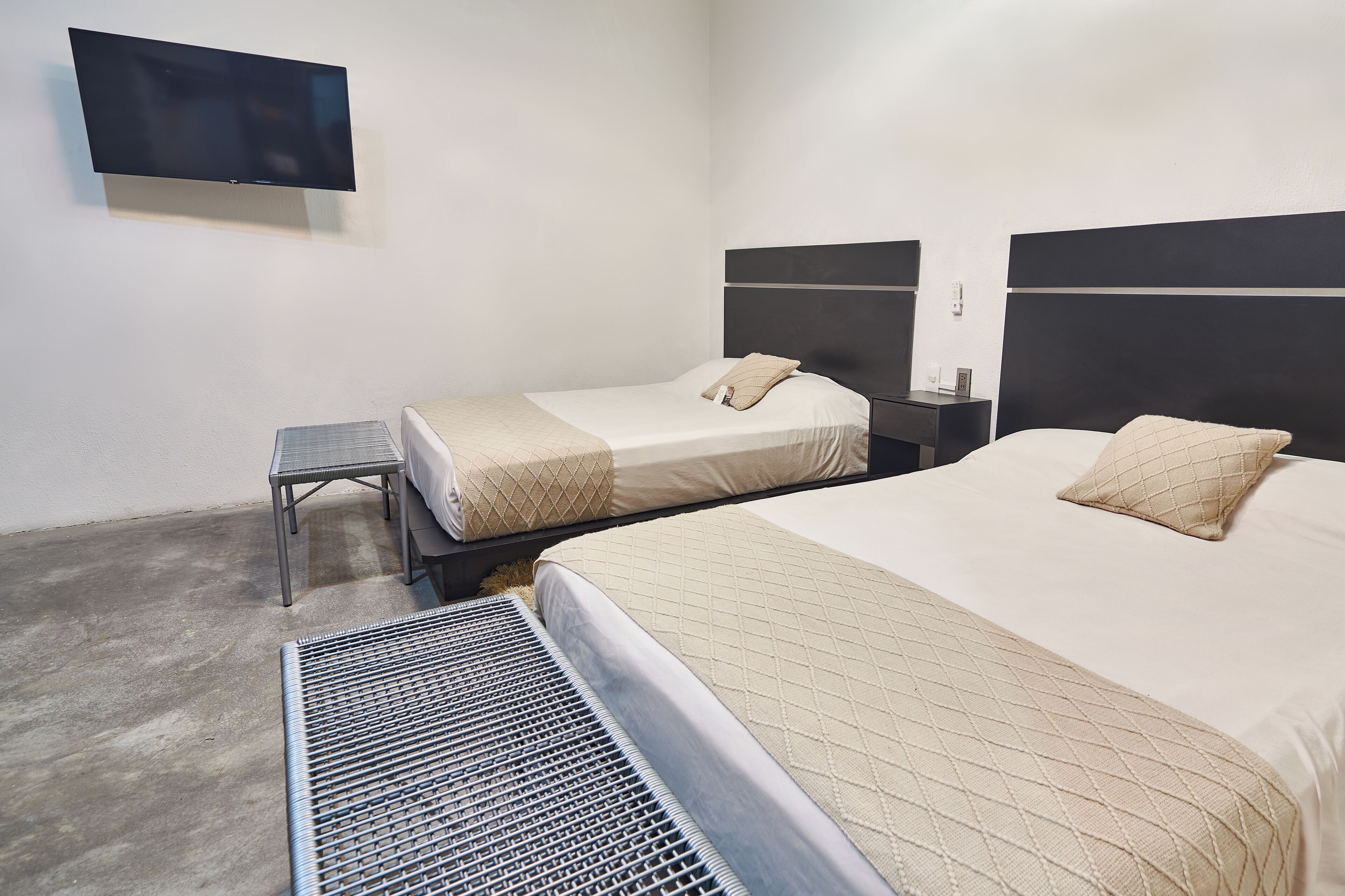 Habitación de hotel con dos camas, un televisor montado en la pared y una mesita.